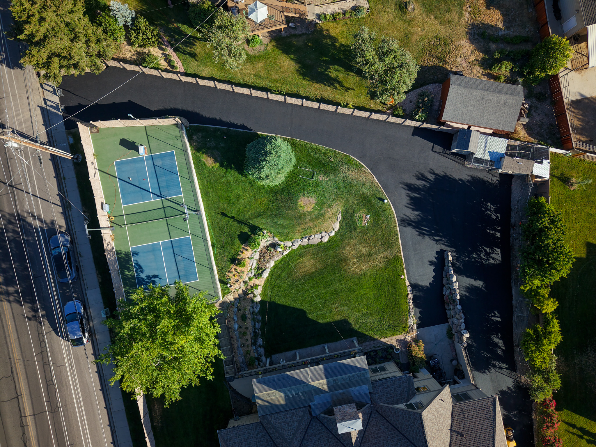 Aerial view of completed curved residential driveway with tennis court and green landscaping